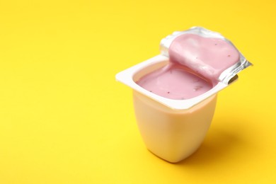 Photo of Delicious yogurt in plastic cup on yellow background, closeup. Space for text