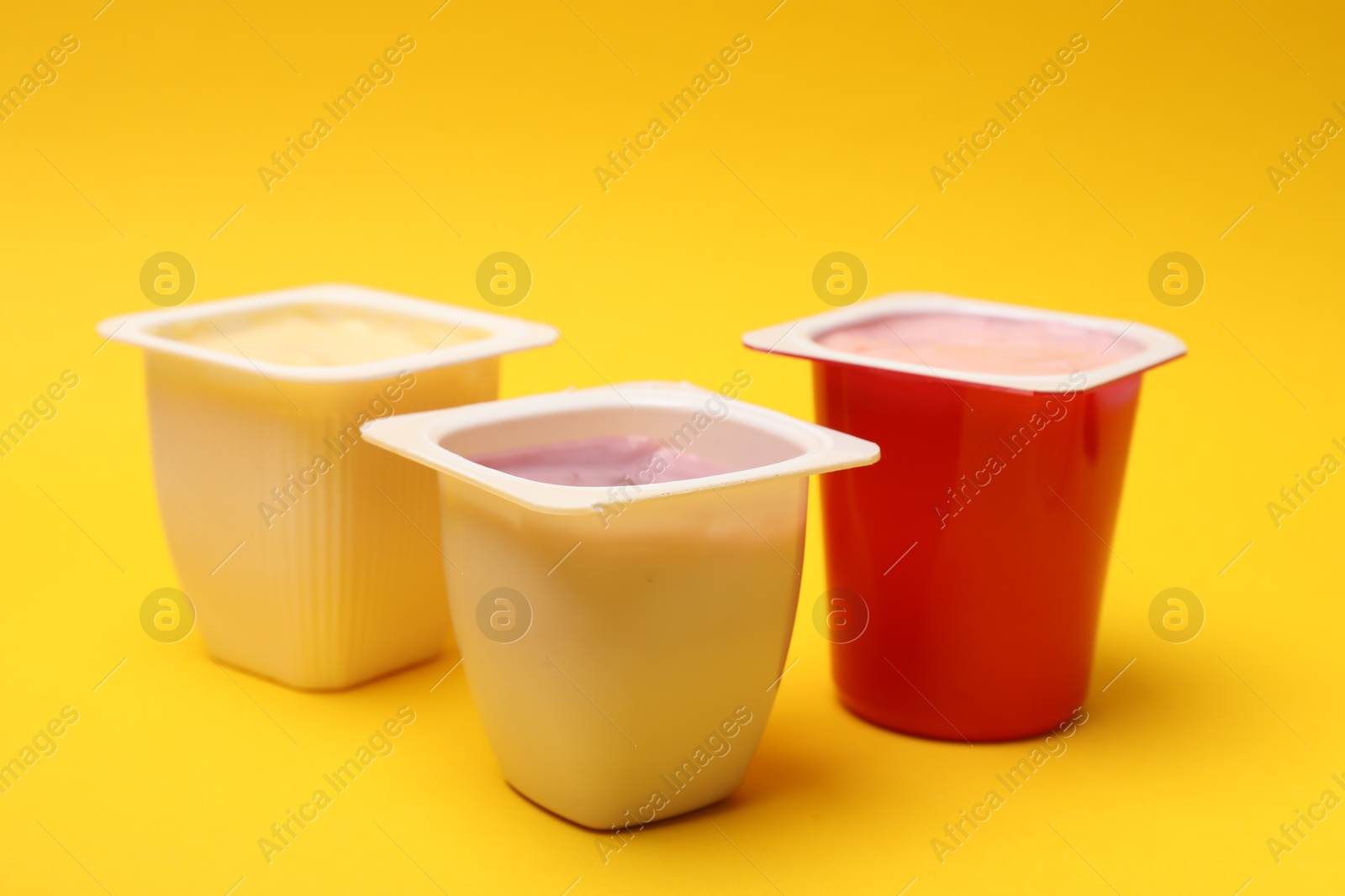 Photo of Delicious yogurts in plastic cups on yellow background, closeup