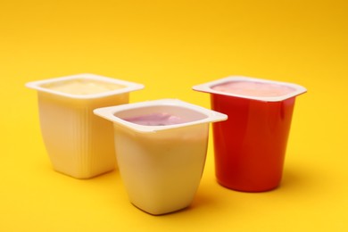 Photo of Delicious yogurts in plastic cups on yellow background, closeup