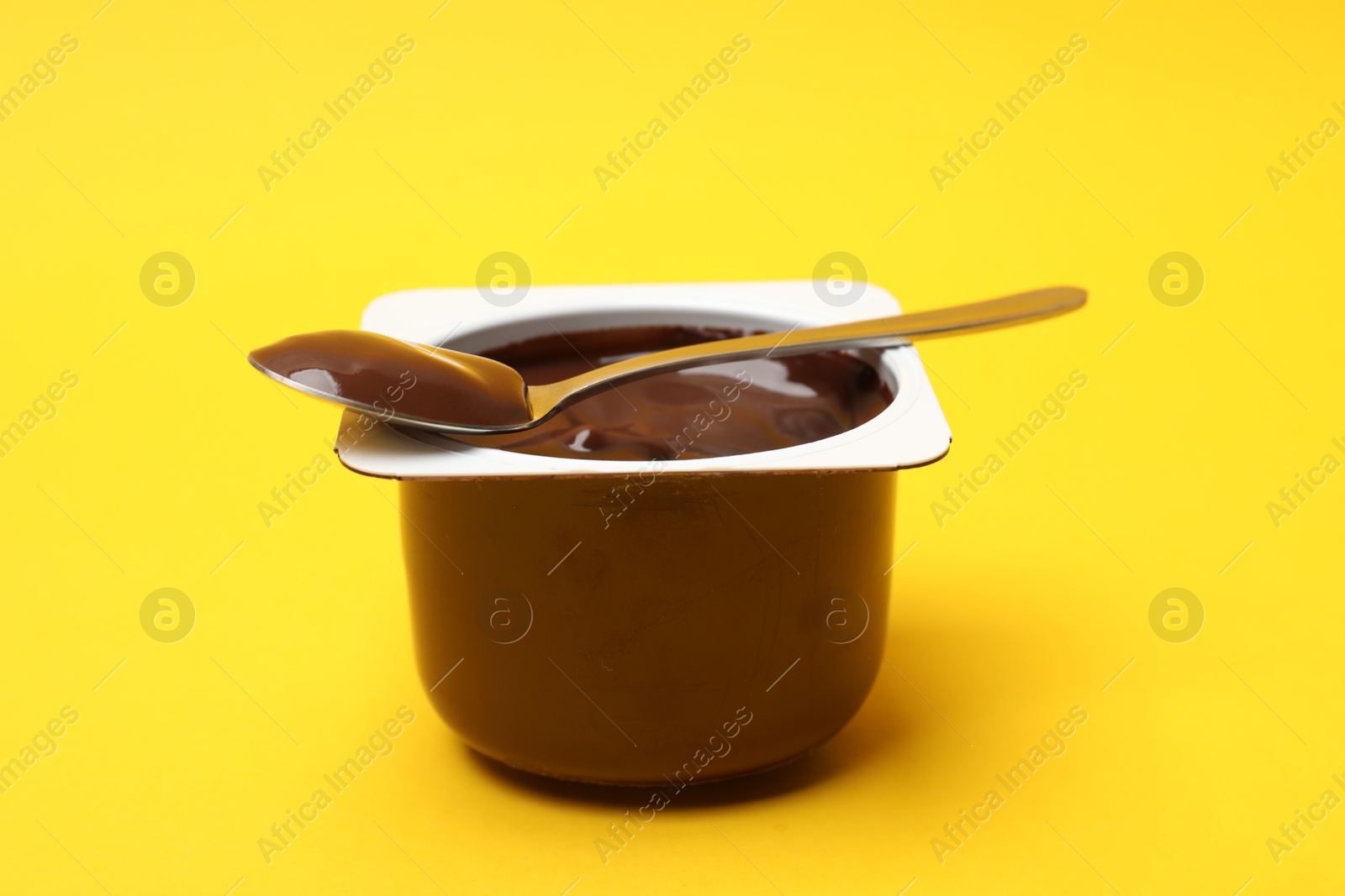 Photo of Delicious chocolate yogurt in plastic cup with spoon on yellow background, closeup