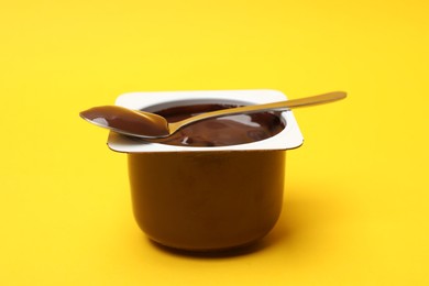 Photo of Delicious chocolate yogurt in plastic cup with spoon on yellow background, closeup