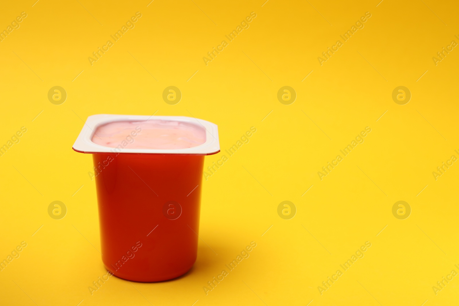 Photo of Delicious yogurt in plastic cup on yellow background, space for text