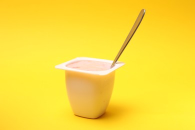 Photo of Delicious yogurt in plastic cup with spoon on yellow background