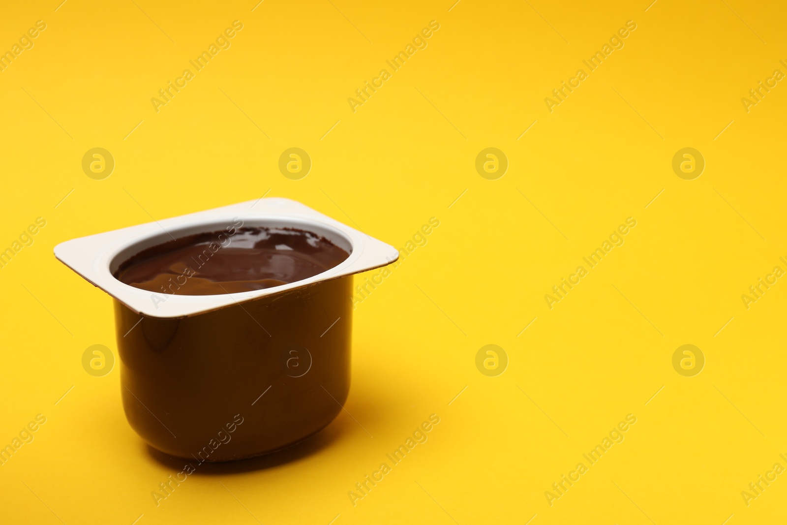 Photo of Delicious chocolate yogurt in plastic cup on yellow background, space for text