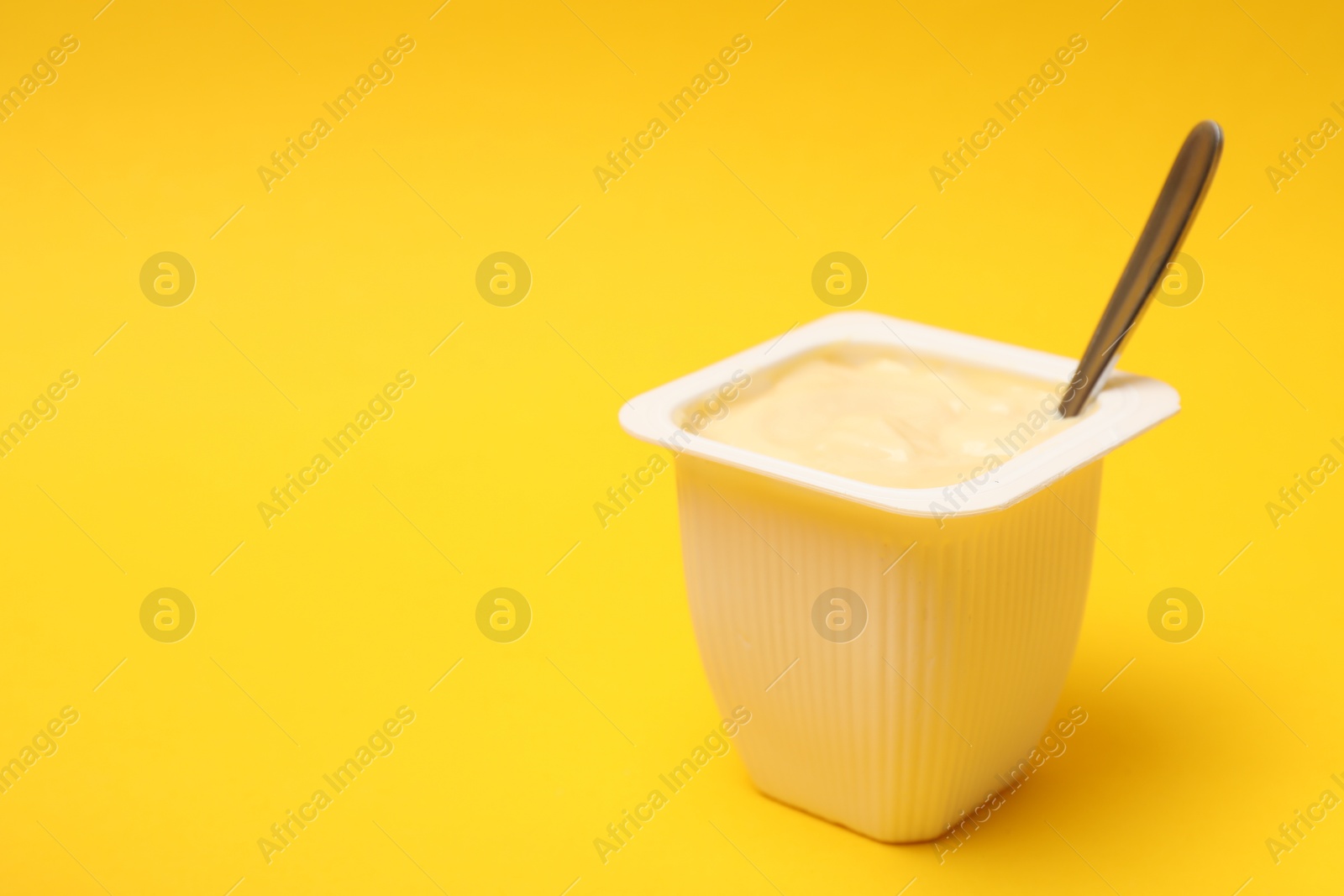 Photo of Delicious yogurt in plastic cup on yellow background, closeup. Space for text