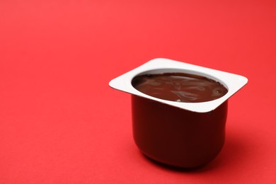 Photo of Delicious chocolate yogurt in plastic cup on red background, closeup. Space for text