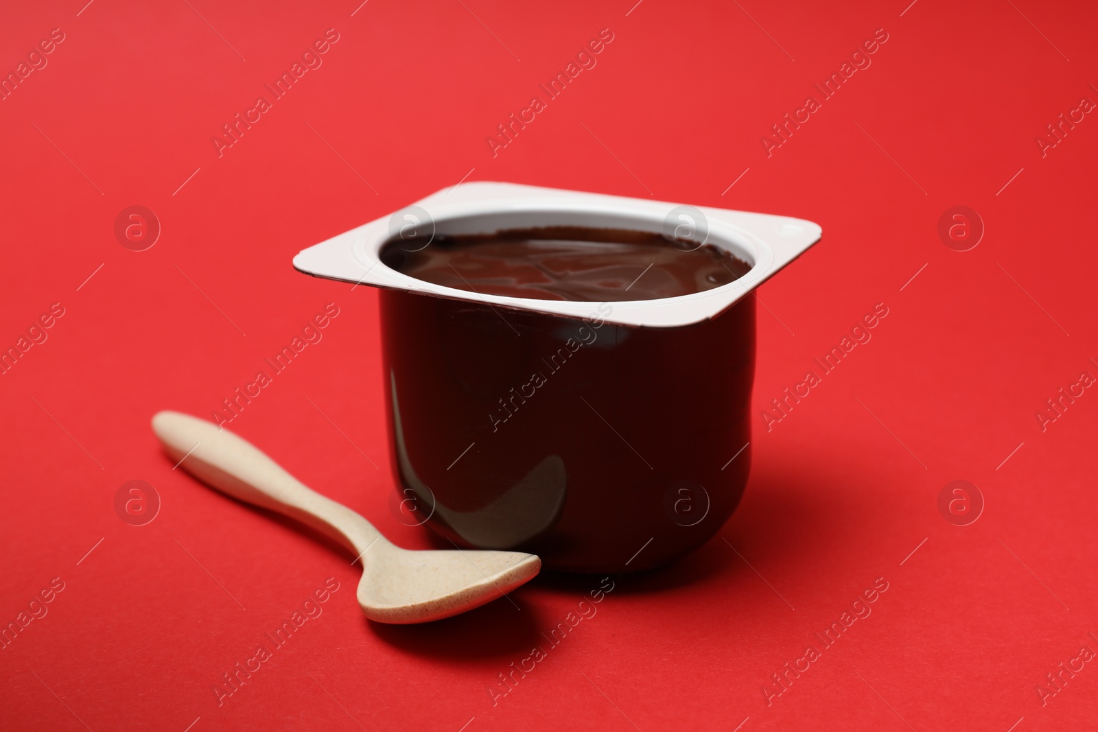 Photo of Delicious chocolate yogurt in plastic cup and spoon on red background, closeup