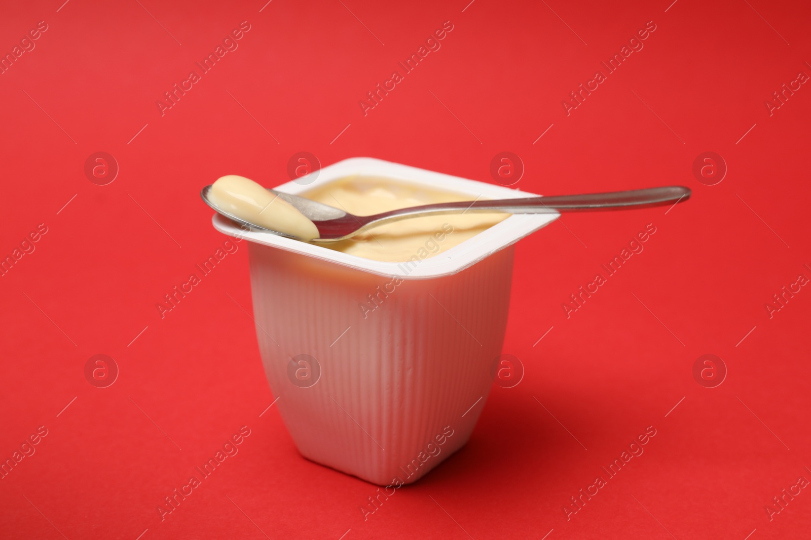 Photo of Delicious yogurt in plastic cup with spoon on red background, closeup