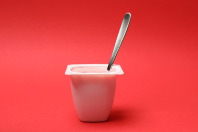 Photo of Delicious yogurt in plastic cup with spoon on red background