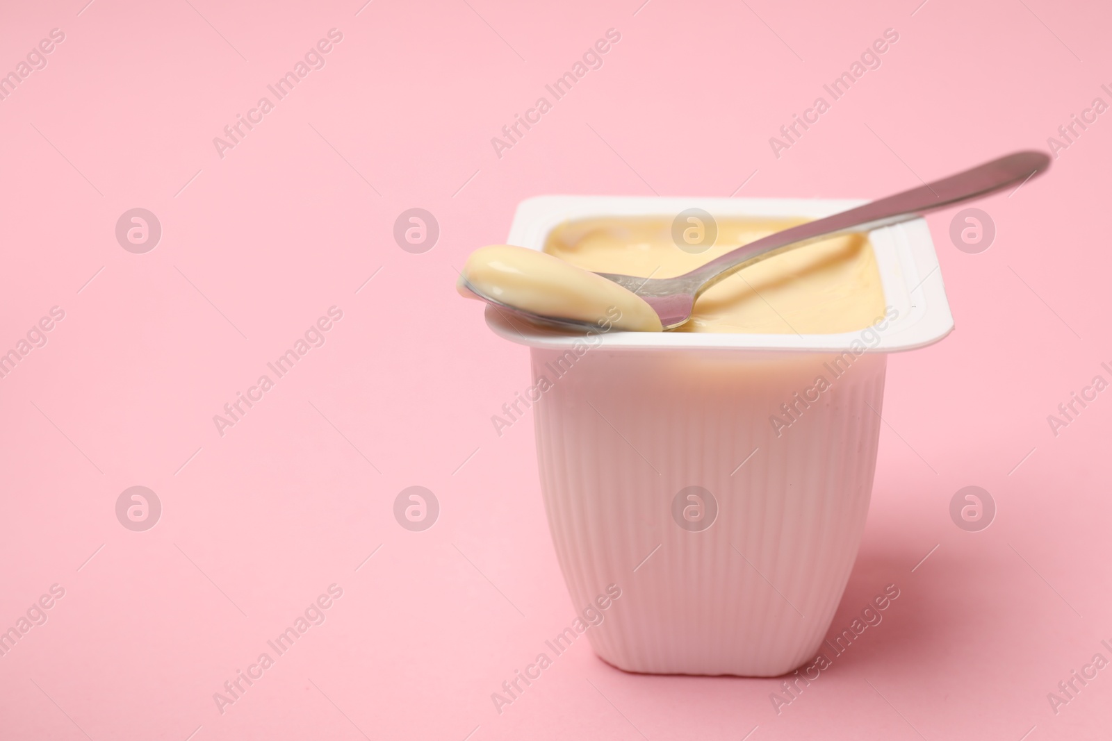 Photo of Delicious yogurt in plastic cup with spoon on pink background, closeup. Space for text