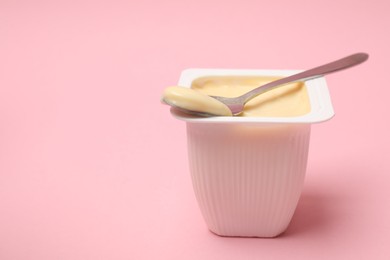 Photo of Delicious yogurt in plastic cup with spoon on pink background, closeup. Space for text