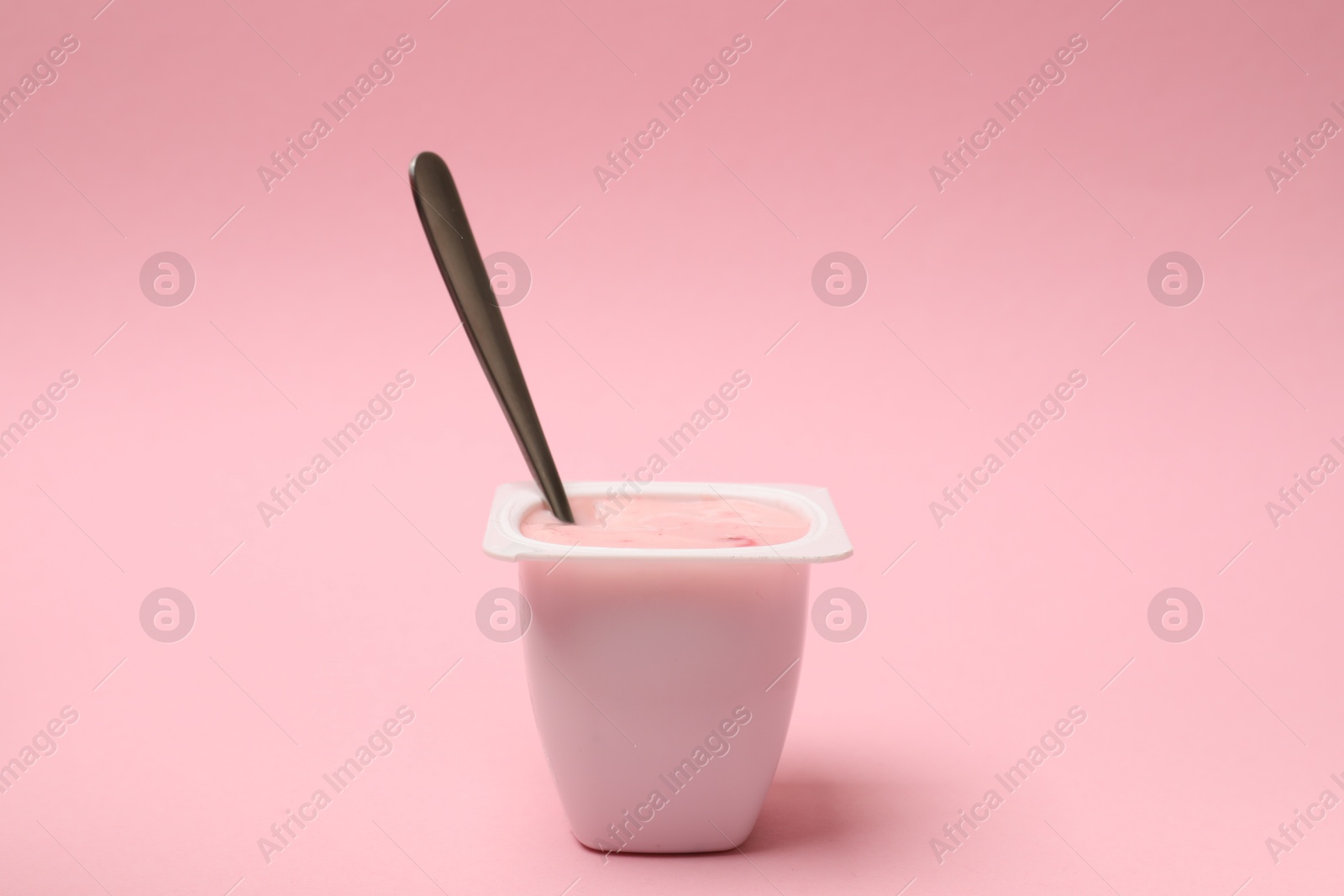 Photo of Delicious yogurt in plastic cup with spoon on pink background