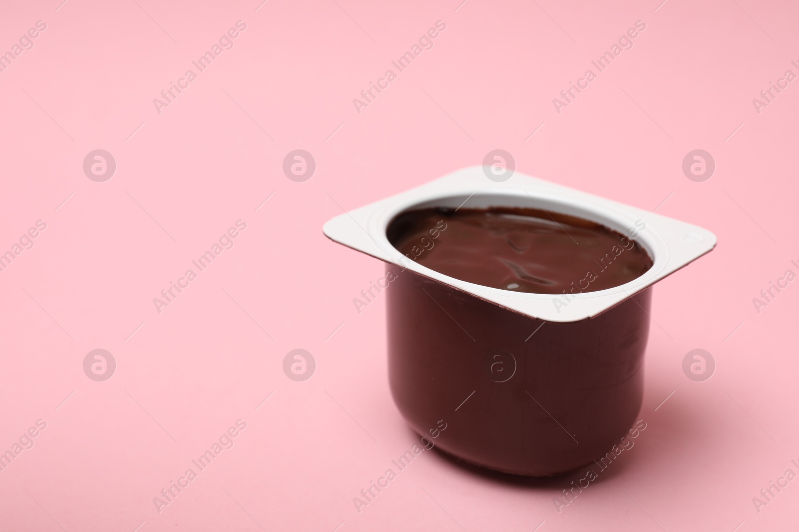 Photo of Delicious chocolate yogurt in plastic cup on pink background, closeup. Space for text