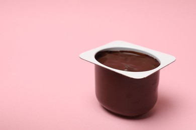 Photo of Delicious chocolate yogurt in plastic cup on pink background, closeup. Space for text