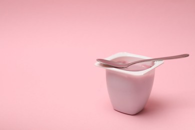 Photo of Delicious yogurt in plastic cup with spoon on pink background, space for text