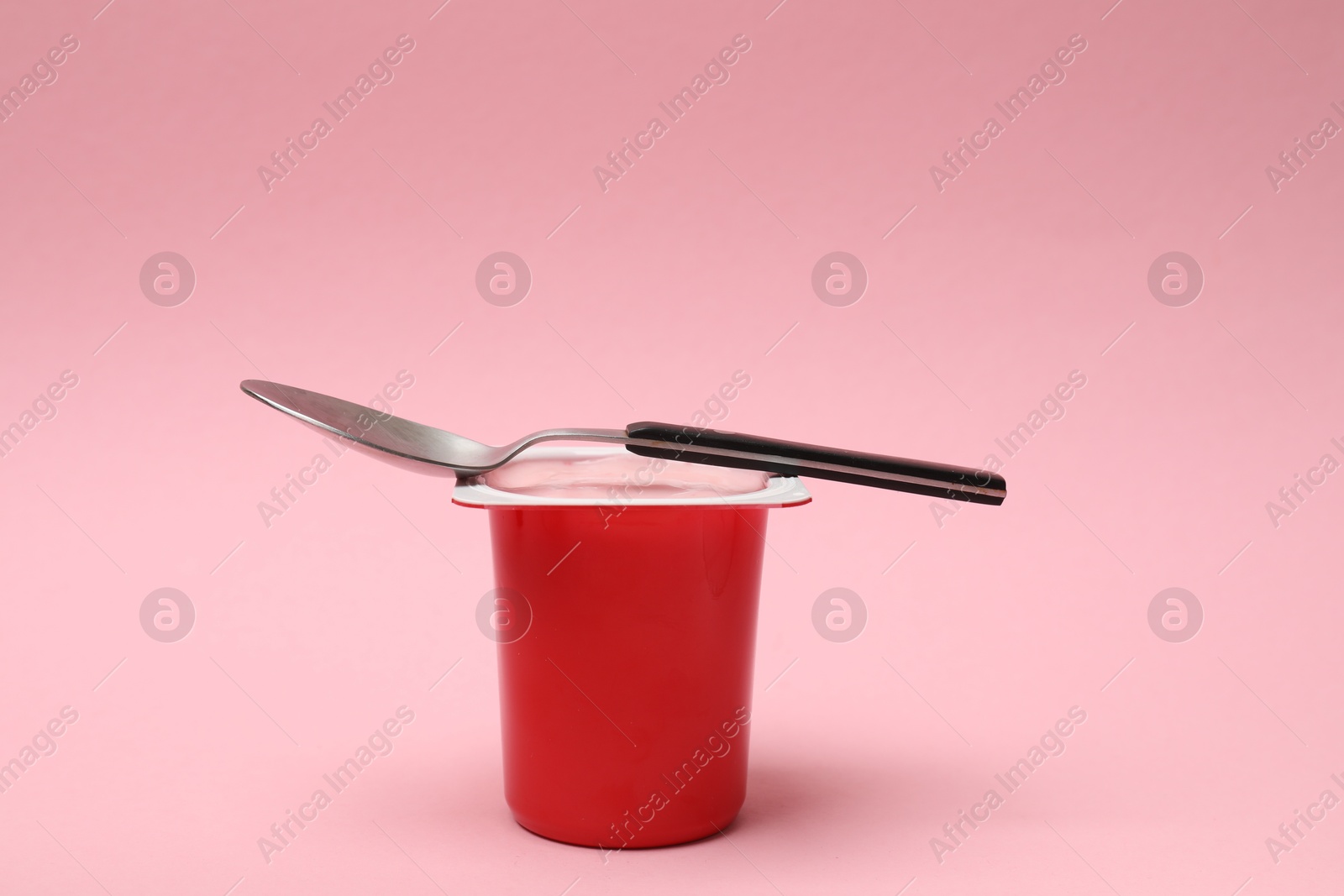 Photo of Delicious yogurt in plastic cup with spoon on pink background