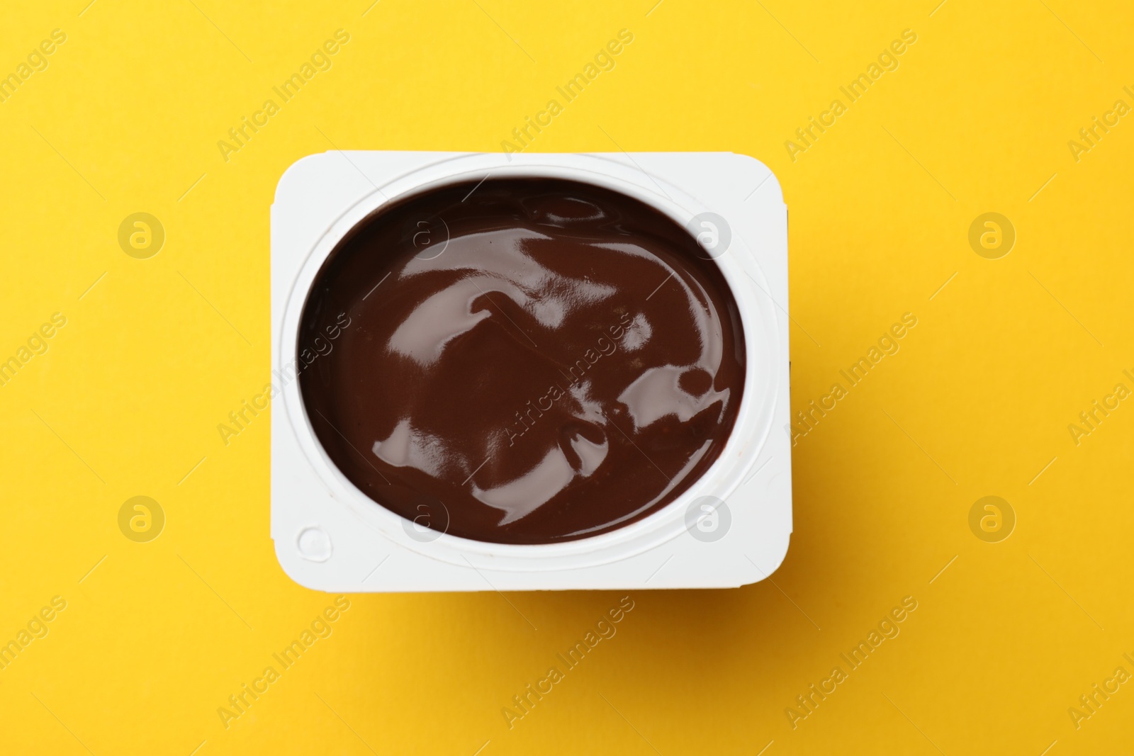 Photo of Delicious chocolate yogurt in plastic cup on yellow background, top view