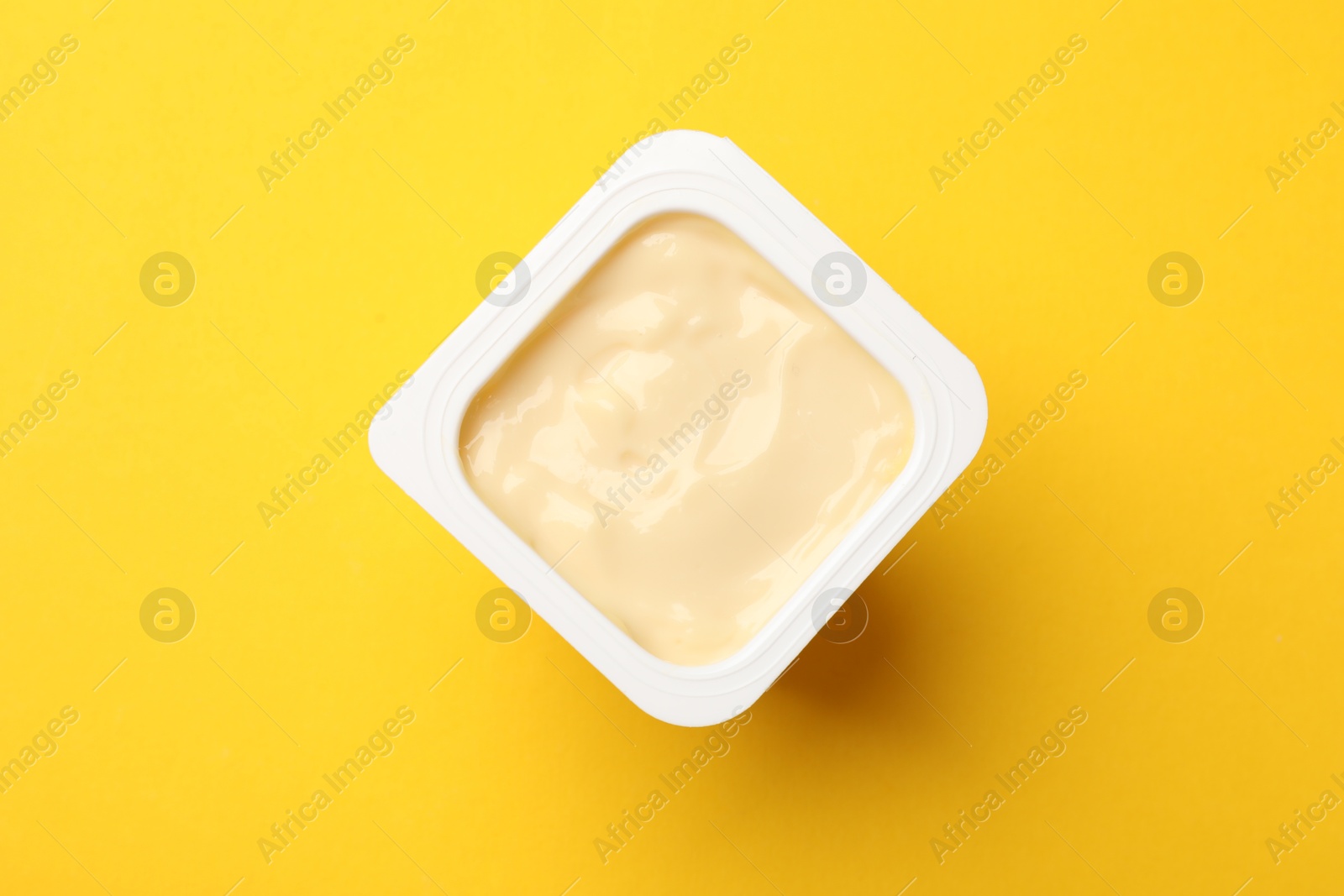 Photo of Delicious yogurt in plastic cup on yellow background, top view