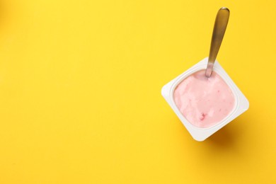 Photo of Delicious yogurt in plastic cup with spoon on yellow background, top view. Space for text