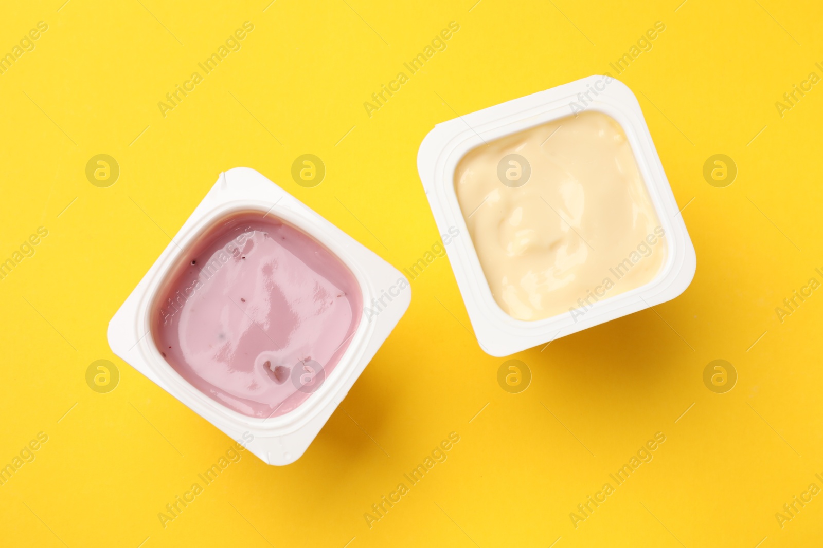 Photo of Delicious yogurts in plastic cups on yellow background, flat lay