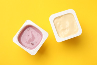 Photo of Delicious yogurts in plastic cups on yellow background, flat lay