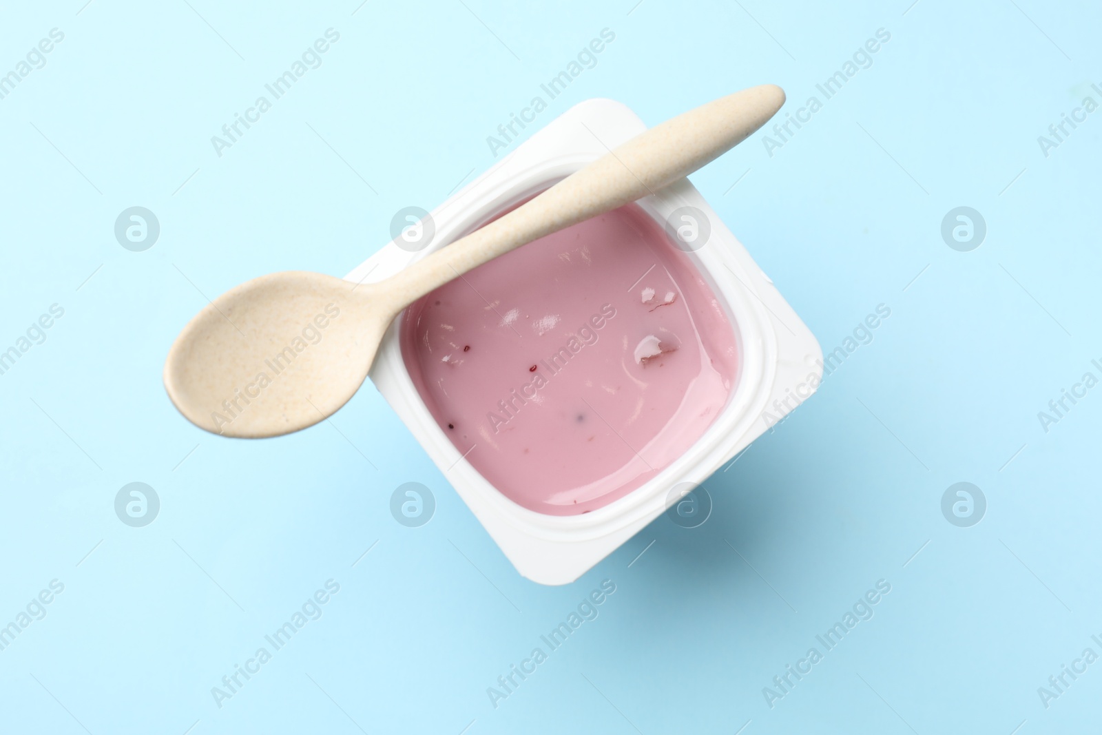 Photo of Delicious yogurt in plastic cup with spoon on light blue background, top view