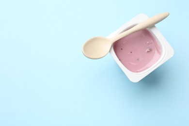 Photo of Delicious yogurt in plastic cup with spoon on light blue background, top view. Space for text