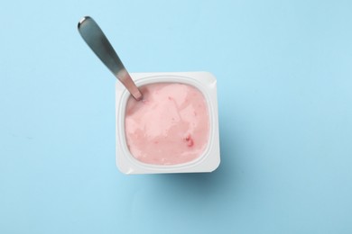 Photo of Delicious yogurt in plastic cup with spoon on light blue background, top view