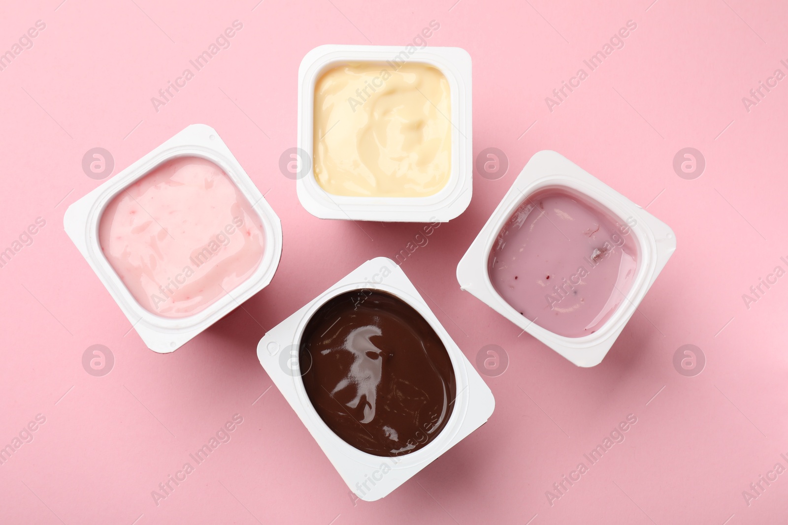 Photo of Delicious yogurts in plastic cups on pink background, flat lay