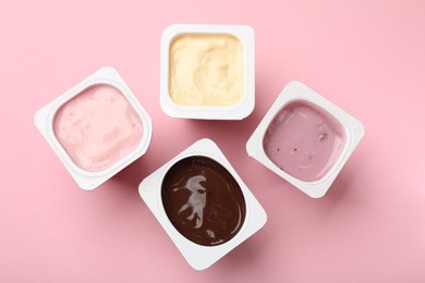 Photo of Delicious yogurts in plastic cups on pink background, flat lay