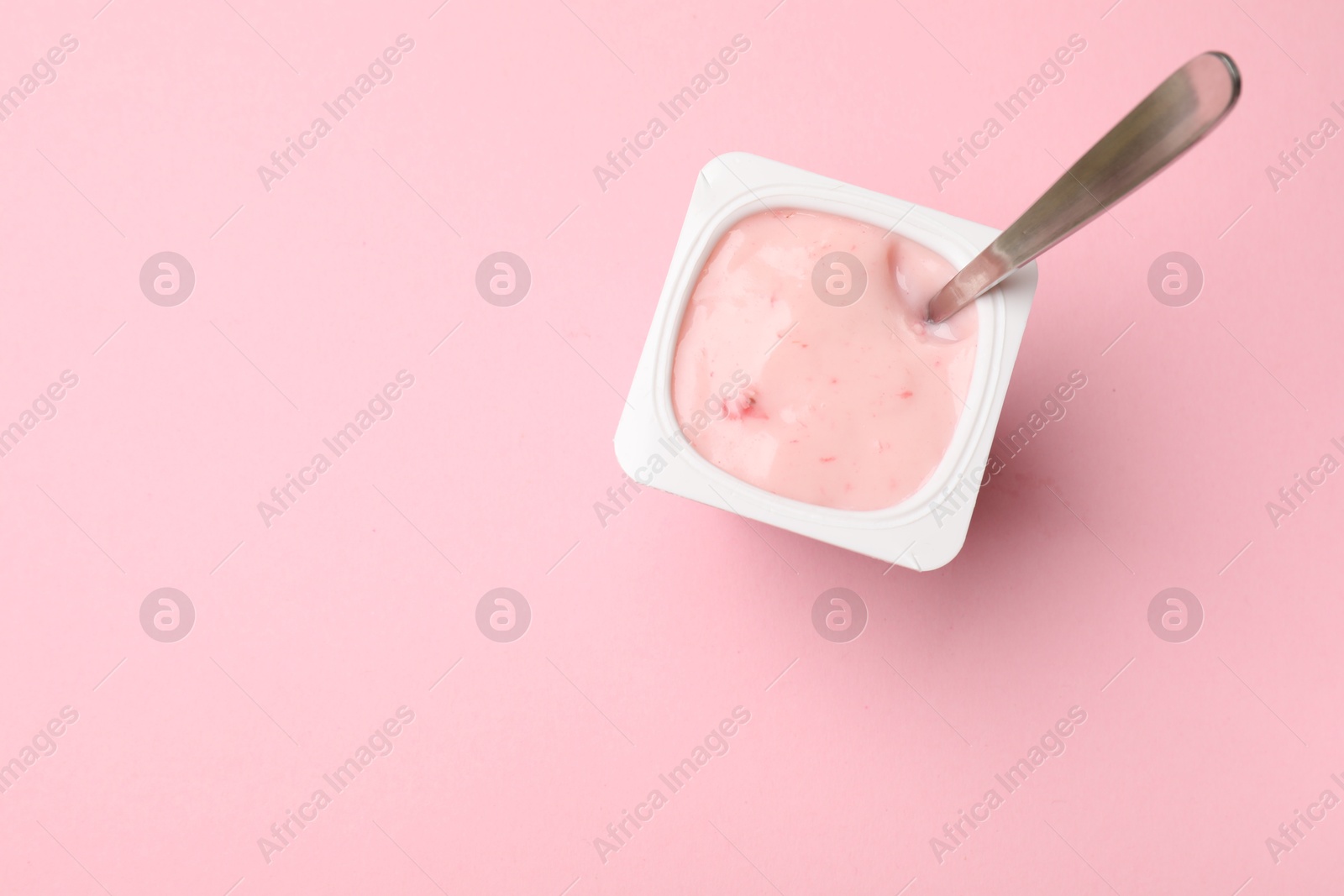 Photo of Delicious yogurt in plastic cup with spoon on pink background, top view. Space for text