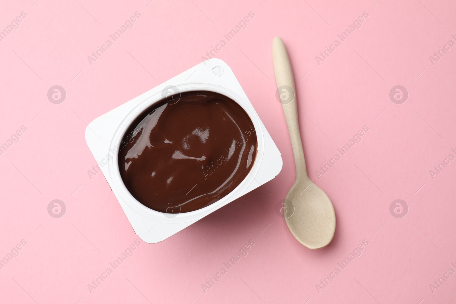 Photo of Delicious chocolate yogurt in plastic cup with spoon on pink background, top view