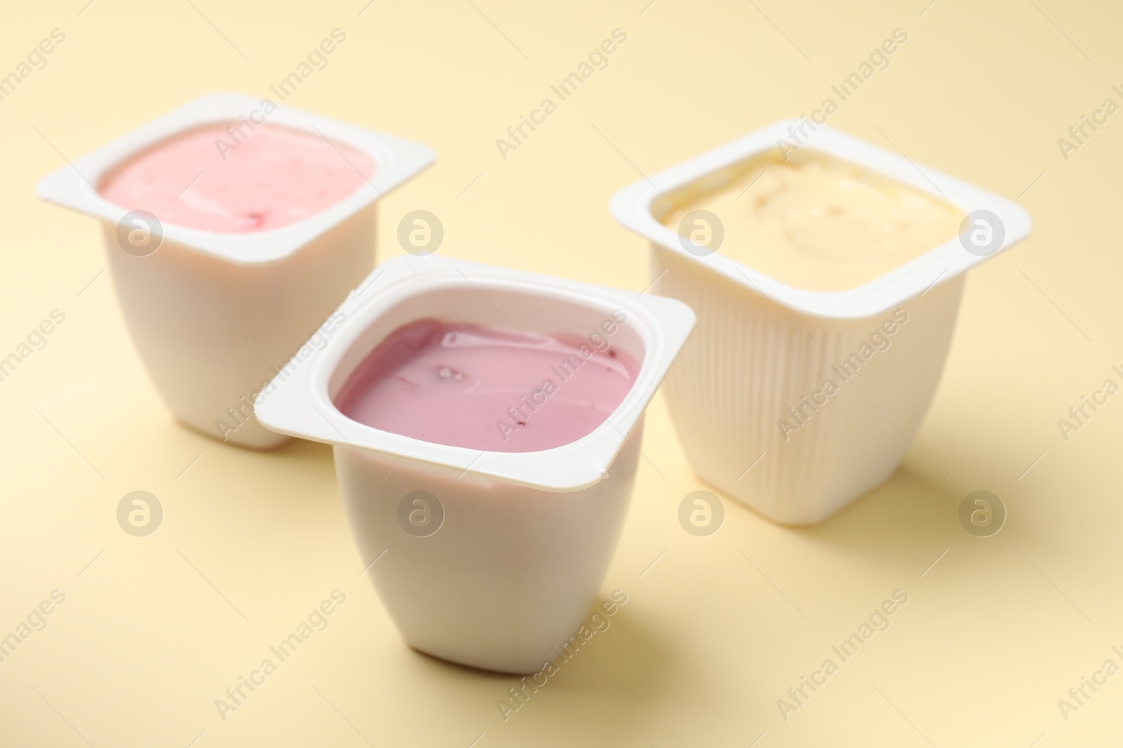 Photo of Delicious yogurts in plastic cups on yellow background, closeup