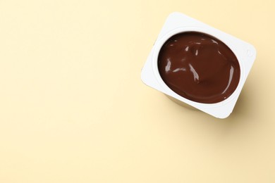 Photo of Delicious chocolate yogurt in plastic cup on yellow background, top view. Space for text