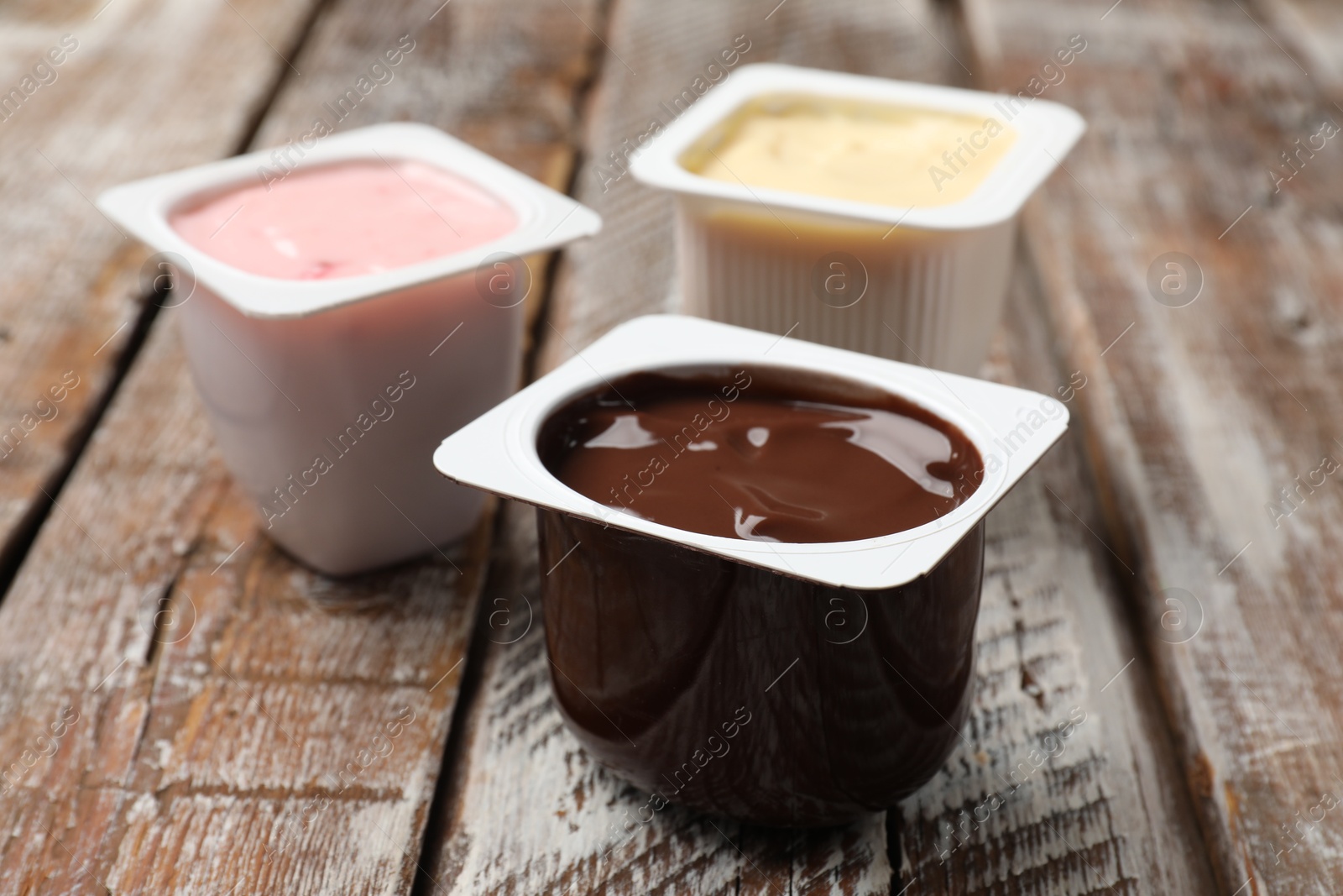 Photo of Delicious yogurts in plastic cups on wooden table, closeup