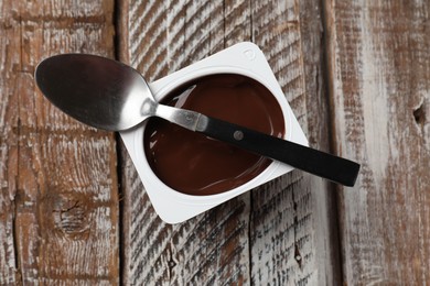 Photo of Delicious chocolate yogurt in plastic cup with spoon on wooden table, top view