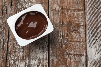 Photo of Delicious chocolate yogurt in plastic cup on wooden table, top view. Space for text