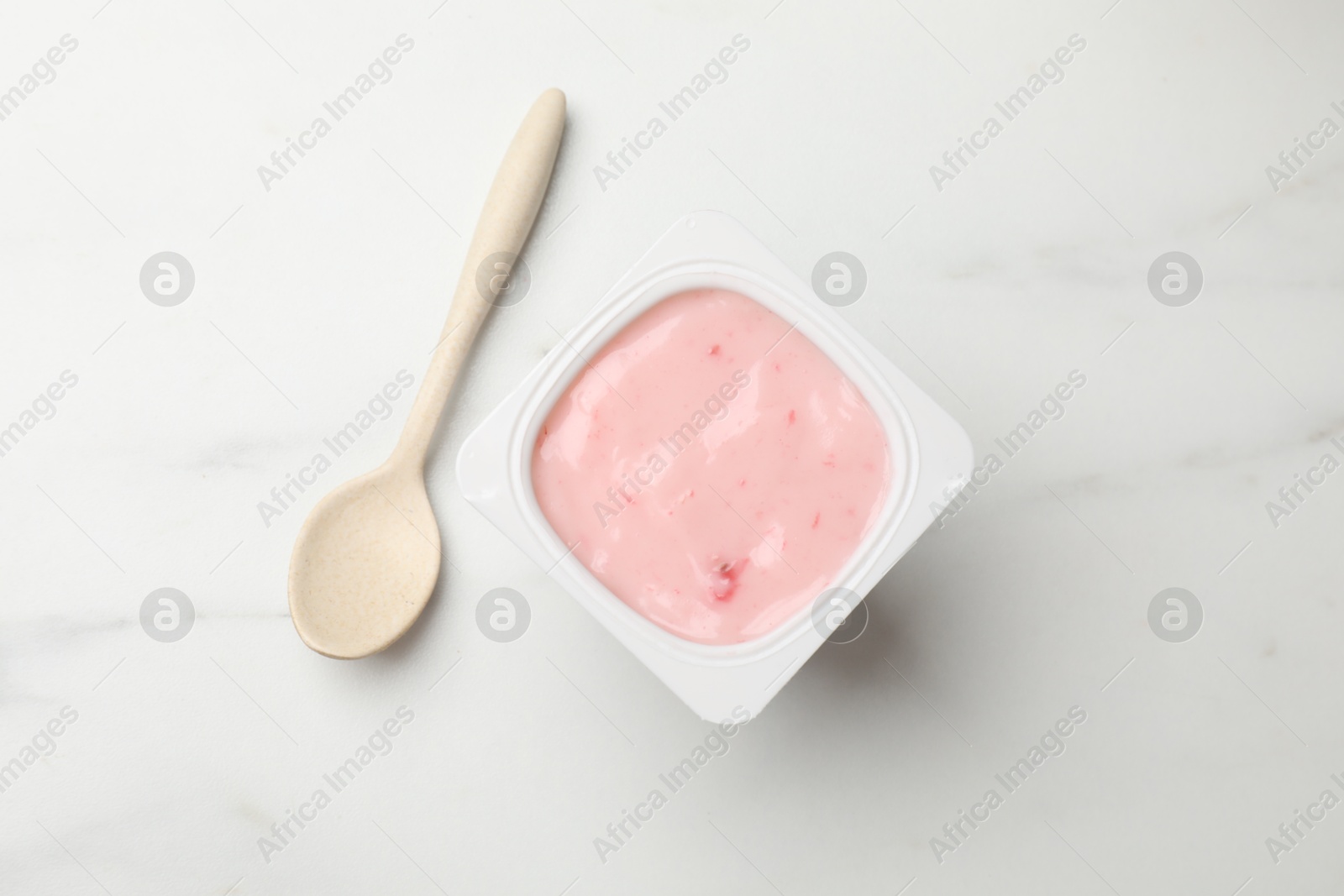 Photo of Delicious yogurt in plastic cup and spoon on light marble table, flat lay