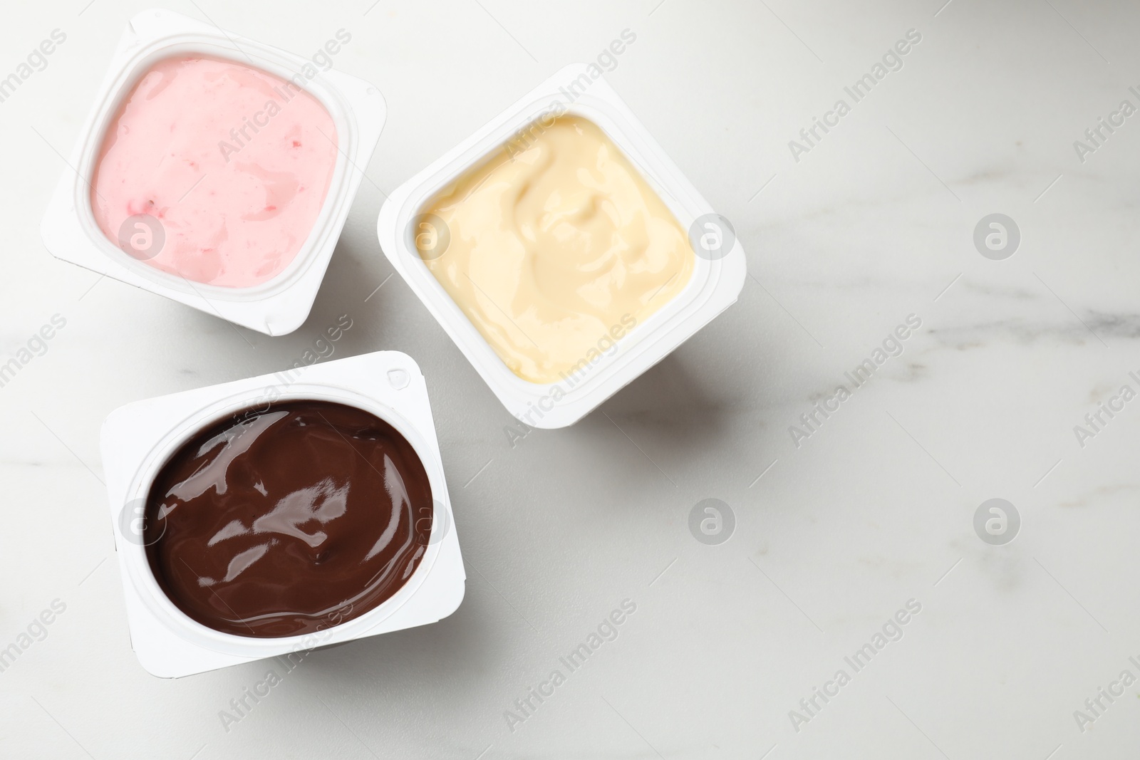 Photo of Delicious yogurts in plastic cups on light marble table, flat lay. Space for text