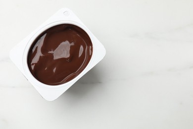 Photo of Delicious chocolate yogurt in plastic cup on light marble table, top view. Space for text