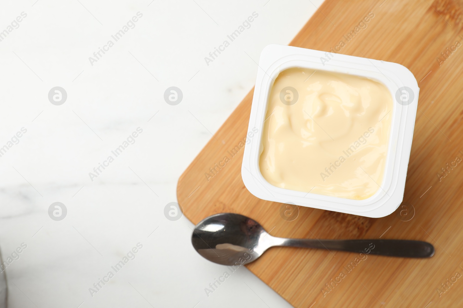 Photo of Delicious yogurt in plastic cup and spoon on light marble table, top view. Space for text