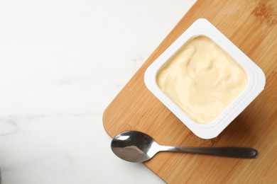 Photo of Delicious yogurt in plastic cup and spoon on light marble table, top view. Space for text