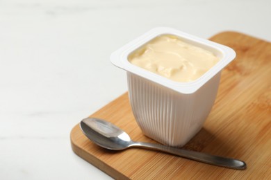 Photo of Delicious yogurt in plastic cup and spoon on light marble table, closeup. Space for text