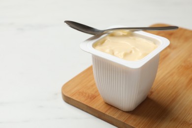 Photo of Delicious yogurt in plastic cup and spoon on light marble table, closeup. Space for text