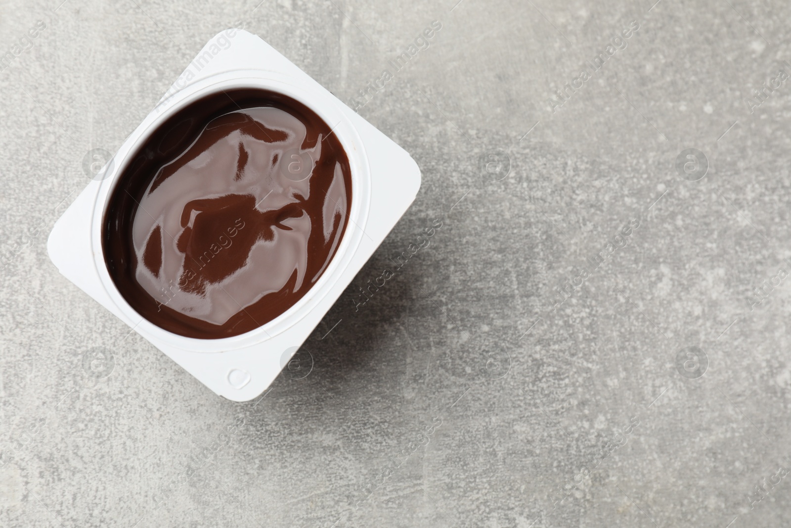 Photo of Delicious chocolate yogurt in plastic cup on gray textured table, top view. Space for text