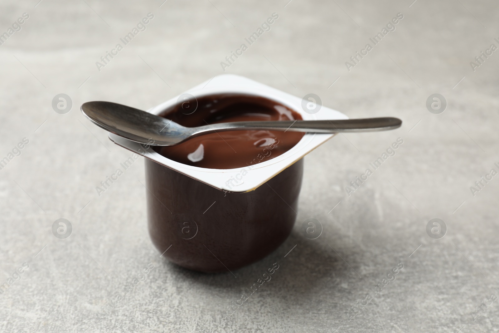 Photo of Delicious chocolate yogurt in plastic cup and spoon on gray textured table, closeup