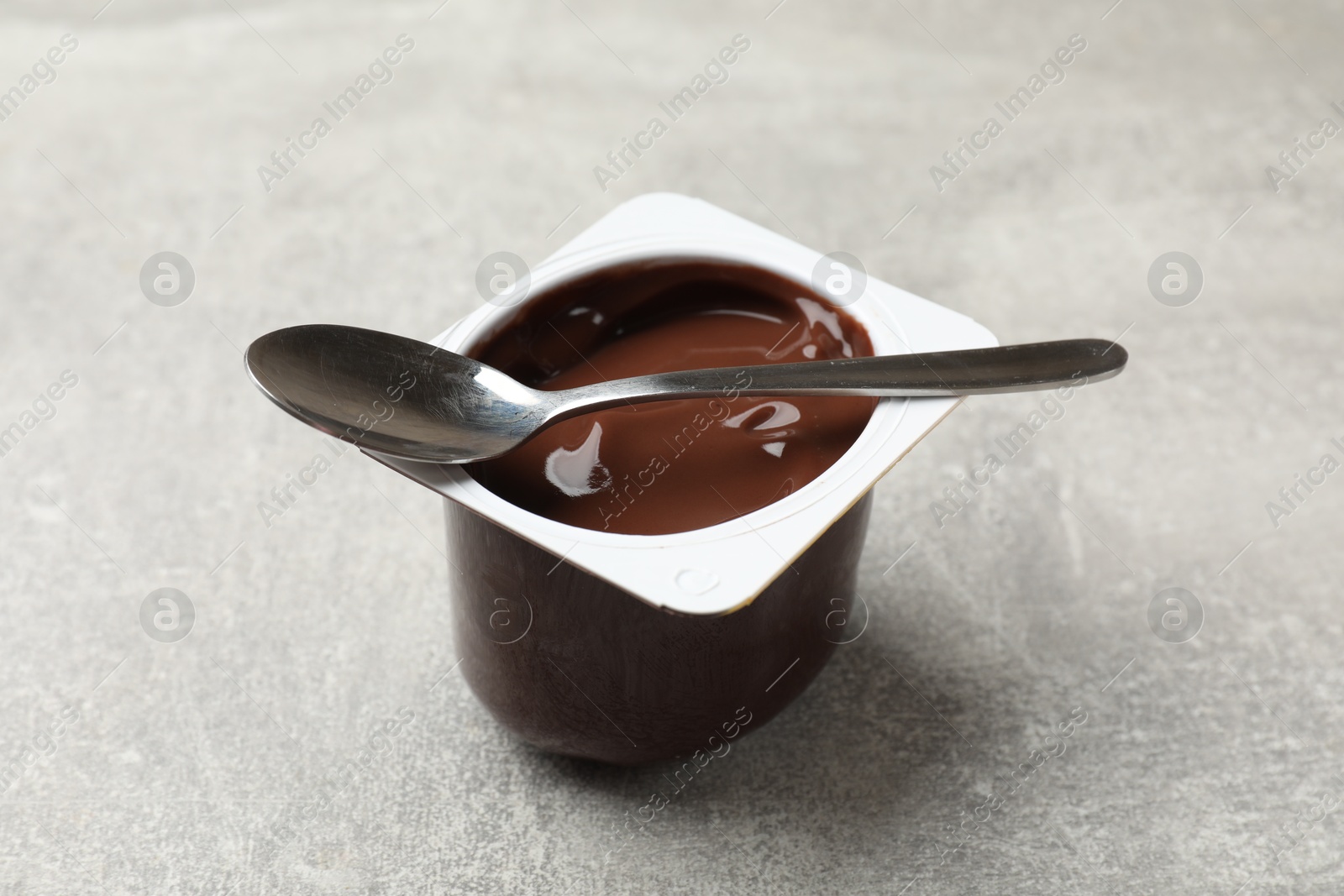 Photo of Delicious chocolate yogurt in plastic cup and spoon on gray textured table, closeup