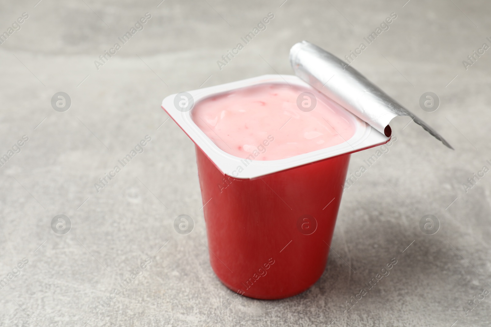 Photo of Delicious yogurt in plastic cup on gray textured table, closeup. Space for text