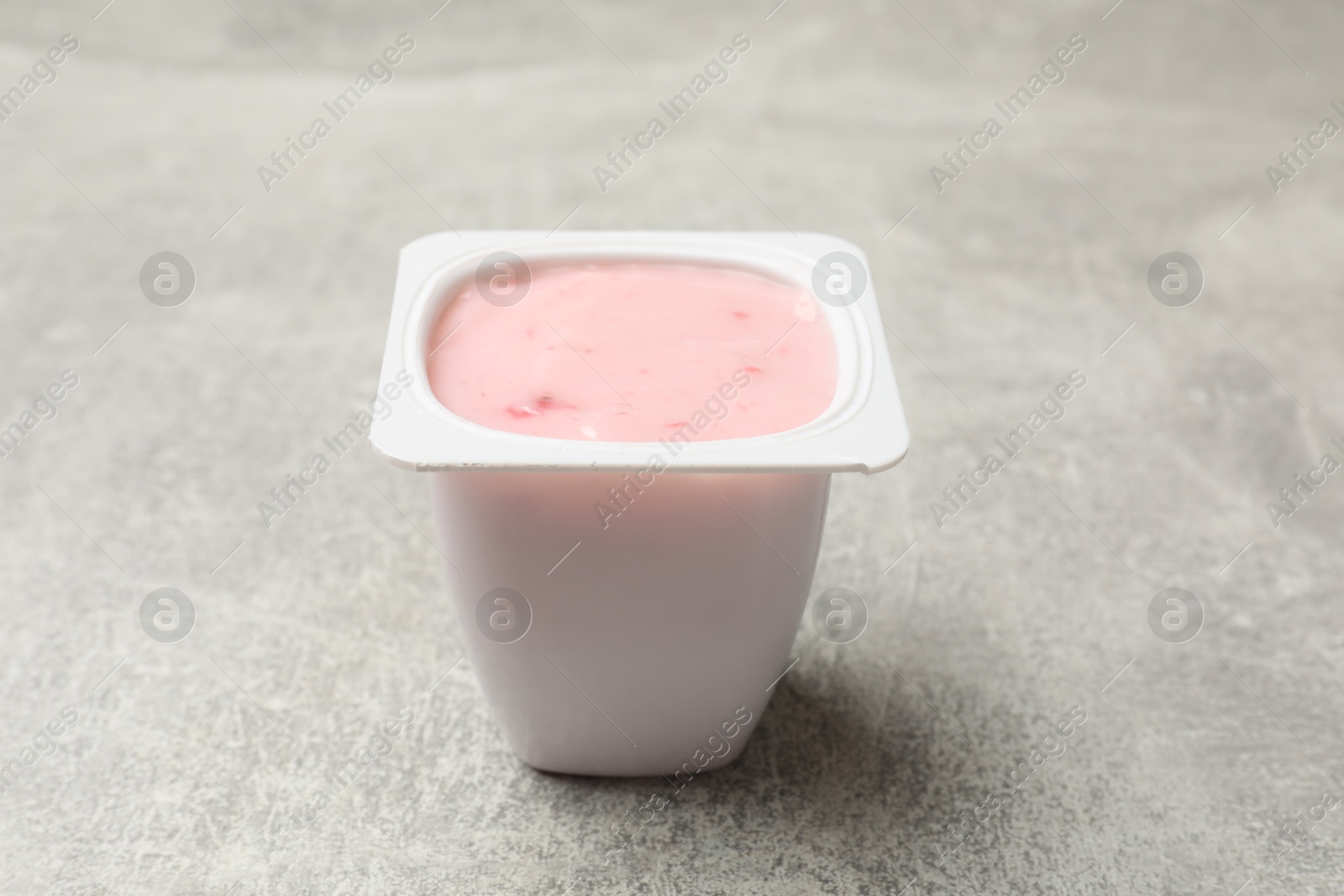 Photo of Delicious yogurt in plastic cup on gray textured table, closeup