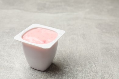 Photo of Delicious yogurt in plastic cup on gray textured table, closeup. Space for text